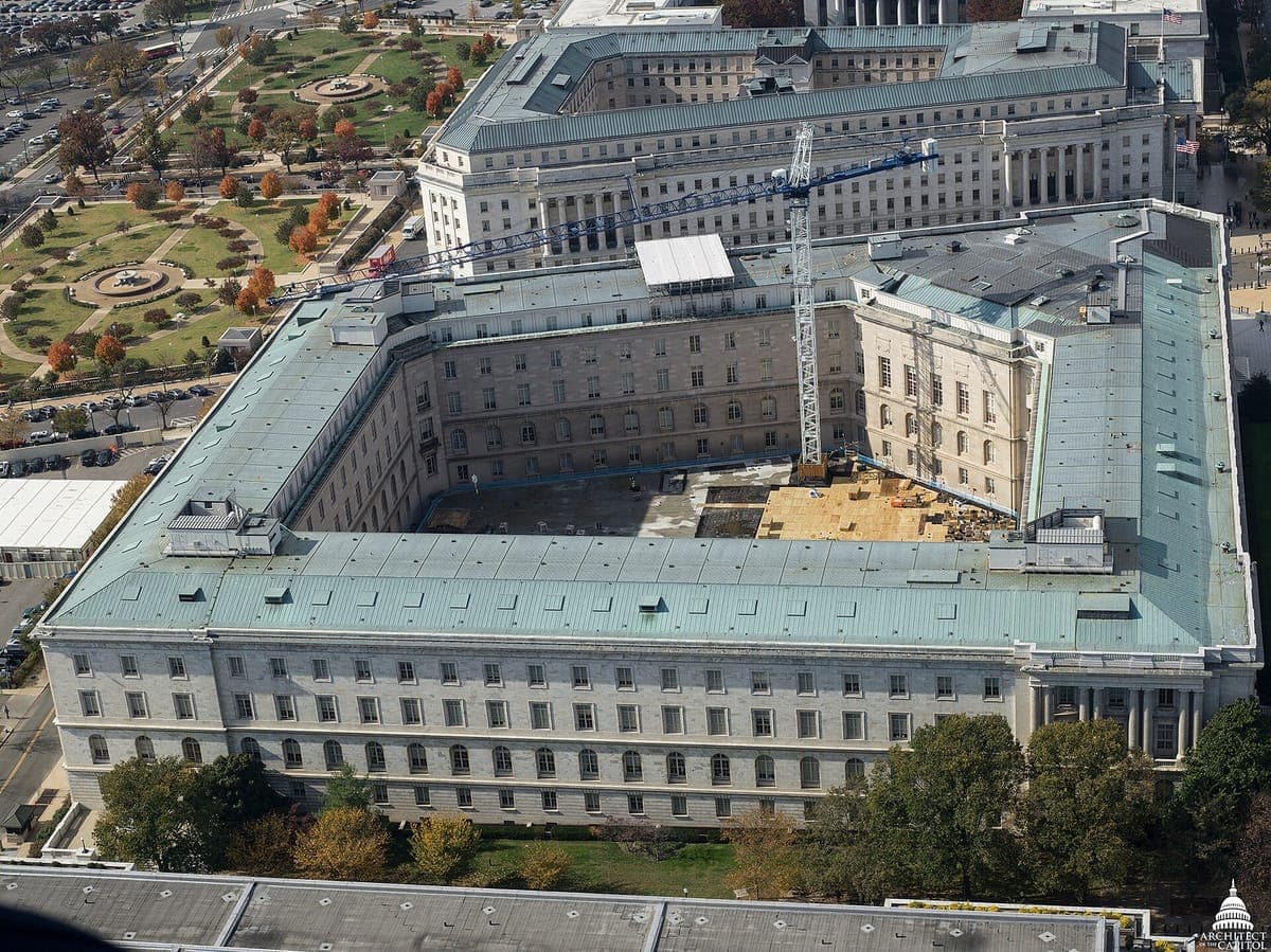 An aerial photo of the Cannon House Office Building in Washington, D.C., a large classical building around a courtyard, with a construction crane and other buildings around it.