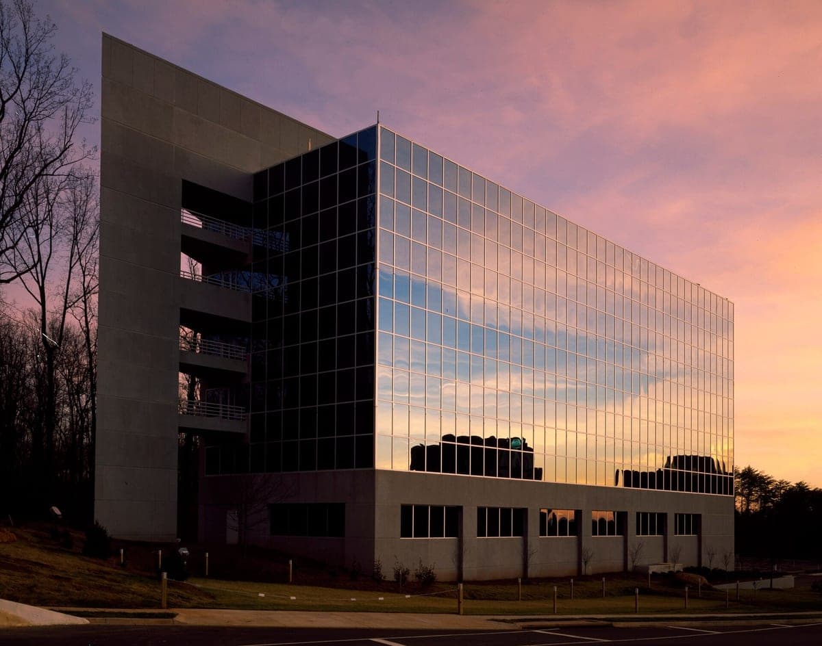 A photo at dusk of a modern office building in northern Virginia: a glass wall reflecting a pink sky, beside a tall pale wall with open balconies.