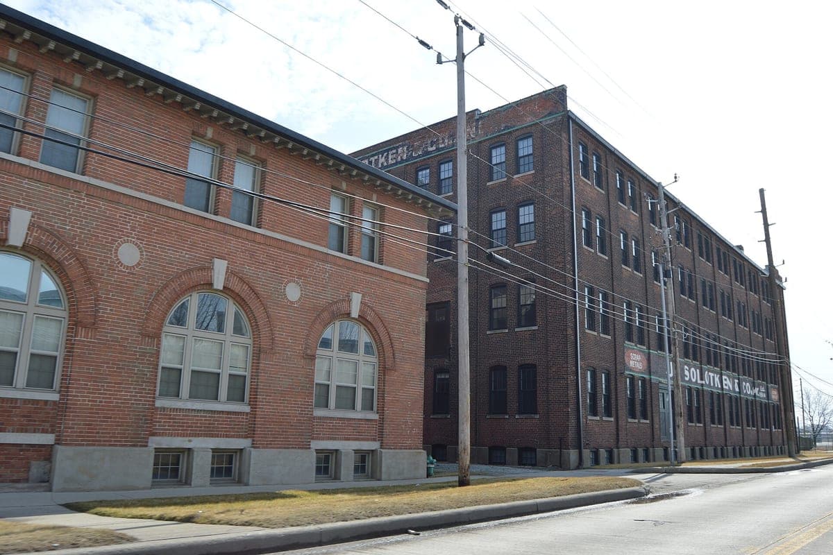 A street photo of a red brick office building in front of a four-story brick warehouse, with utility poles, wires and a faded painted sign.