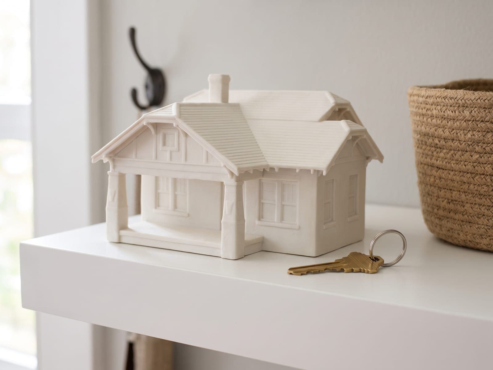 A finished bungalow house piece with a deep front porch, on a white floating shelf in a small entry, a single new key on a ring beside it, in a generated picture