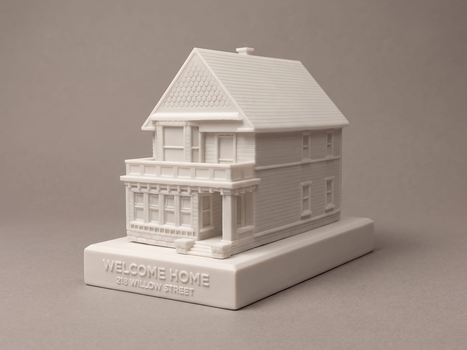 A finished Victorian house piece with a shingled gable and a porch with a balcony above, pictured on a slim base in the same white with raised letters reading Welcome Home, 218 Willow Street, against a plain grey backdrop, in a generated picture