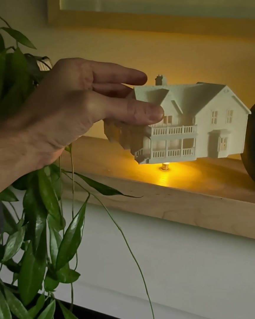 A hand setting a real finished white house piece over its glowing LED light on a wood shelf