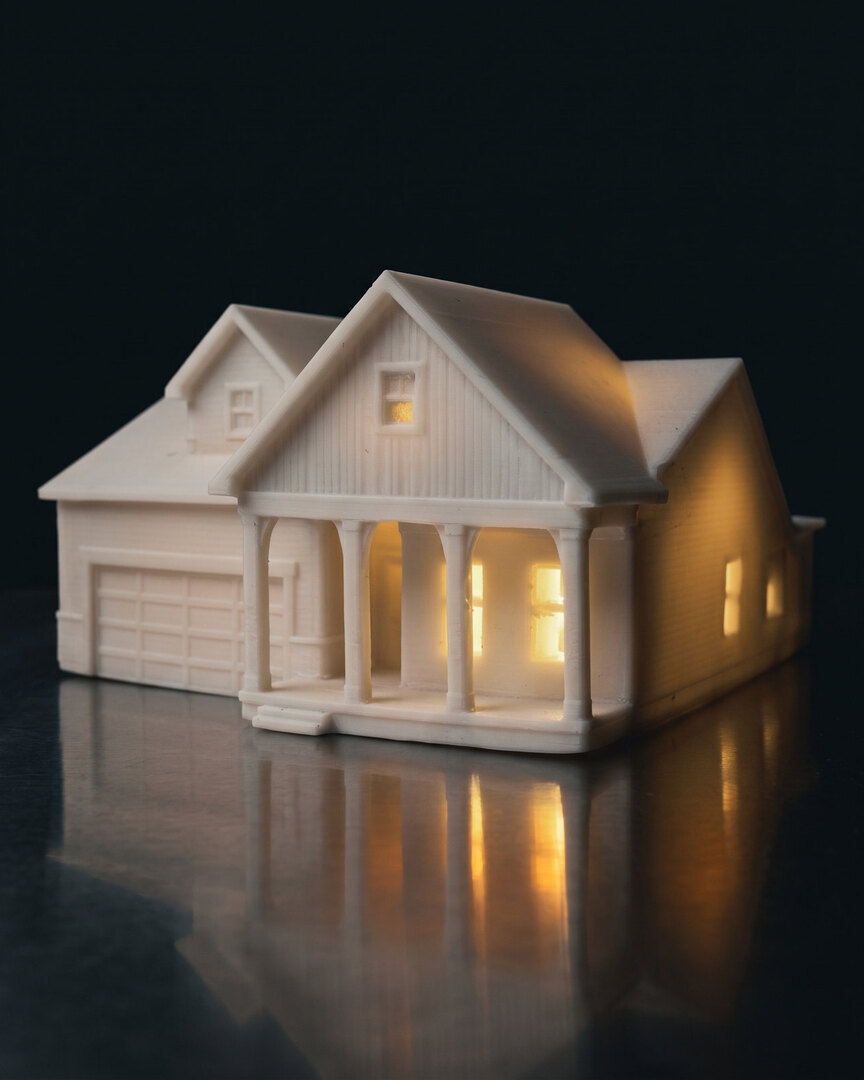 A real finished white farmhouse piece with a garage and front porch, glowing from inside on brushed steel