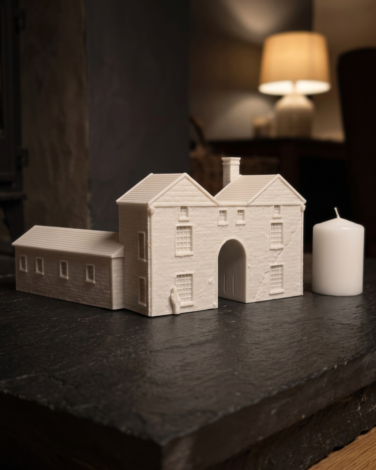 A finished white stone house piece with an arched carriage gate on a slate board in a dim room, in a generated picture