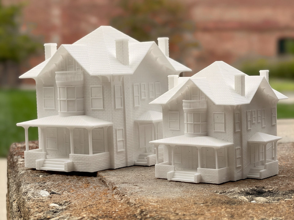 Two finished Victorian house keepsakes in two sizes on a stone ledge, a brick courtyard behind them